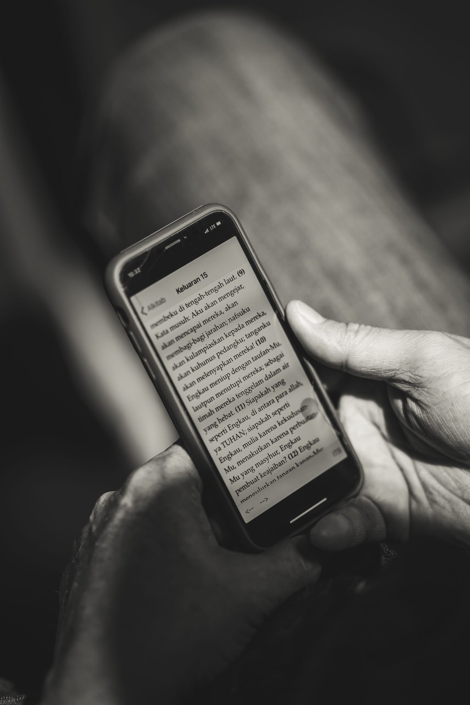 Monochrome photo of hands holding a smartphone displaying text indoors. Perfect for illustrating technology use.